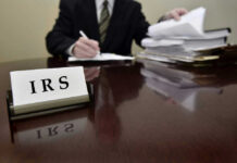 IRS sign on desk, person handling paperwork behind