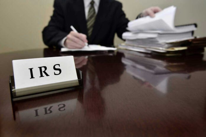 shutterstock_158874281.jpg IRS sign on desk, person handling paperwork behind