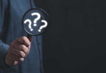 Hand holding magnifying glass with question marks