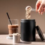 Protein Powders Poisoning American Families? Hand pouring protein powder into a container next to a glass of iced coffee