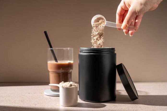 Hand pouring protein powder into a container next to a glass of iced coffee