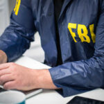 Person in FBI jacket working on laptop.