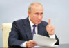 Vladimir Putin, holding papers, in a meeting.