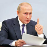 Vladimir Putin, holding papers, in a meeting.