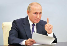 Vladimir Putin, holding papers, in a meeting.