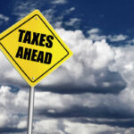 Energy Tax Plan Sparks Panic Yellow road sign reading taxes ahead clouds background