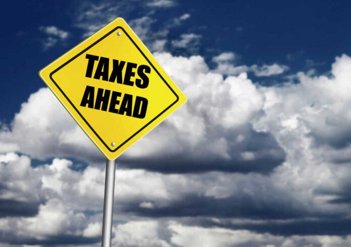Yellow road sign reading taxes ahead clouds background