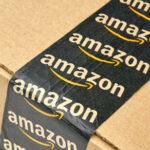 Amazon’s AI Gamble — Engineers Axed By The Thousands Close-up of an Amazon-branded shipping box tape on a cardboard box