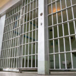 Empty prison cell with metal bars and toilet.
