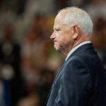 MASSIVE Theft Under Tim Walz — Taxpayers STUNNED Tim Walz in a suit standing before audience.