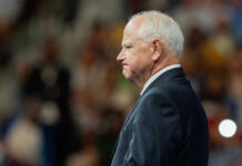 MASSIVE Theft Under Tim Walz — Taxpayers STUNNED Tim Walz in a suit standing before audience.