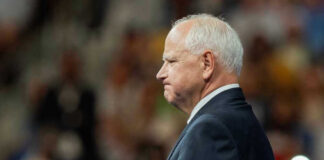 Tim Walz in a suit standing before audience.