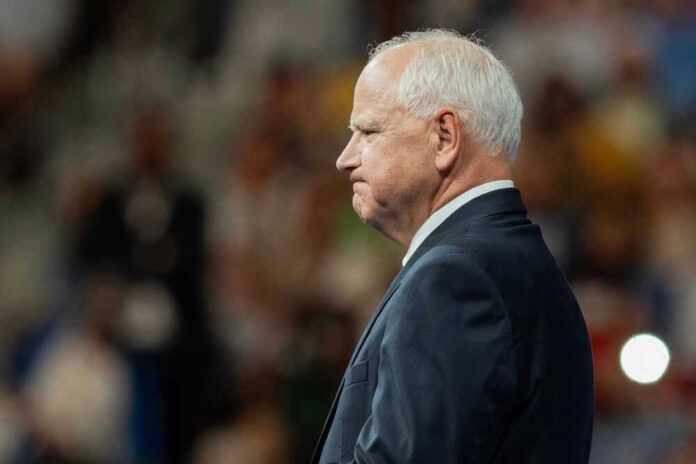 shutterstock_2499464649.jpg Tim Walz in a suit standing before audience.
