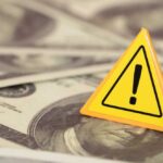A yellow warning sign on a background of dollar bills