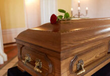 A wooden casket with a red rose placed on top