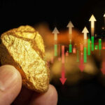 Hand holding gold nugget with financial market chart.