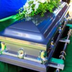 A silver casket adorned with flowers at a gravesite