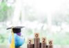 Globe with a graduation cap next to stacks of coins and wooden blocks displaying the year 2026