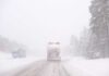 Two trucks driving on a snowy road during a blizzard