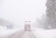 Two trucks driving on a snowy road during a blizzard