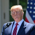 SHOCKING Defeat: Trump Forced to Withdraw Donald Trump speaking with US flag in the back.