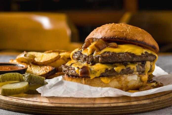 shutterstock_2594563079.jpg A double cheeseburger with melted cheese and pickles served with potato wedges