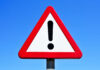 A triangular warning sign with an exclamation mark against a blue sky