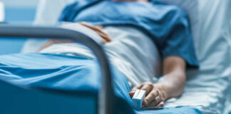 A patient lying in a hospital bed with a monitoring device in hand