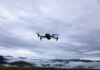 A drone flying against a cloudy sky over a mountainous landscape