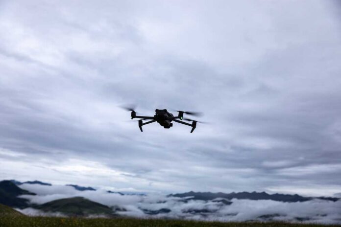 shutterstock_2487499353.jpg A drone flying against a cloudy sky over a mountainous landscape