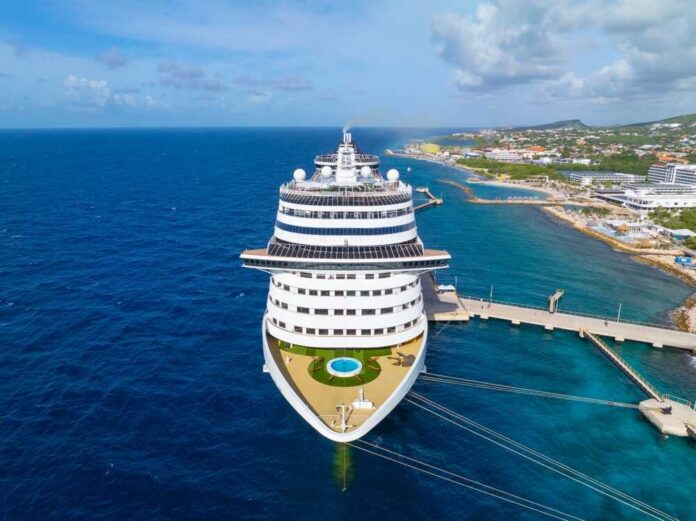 shutterstock_2556351301.jpg A large cruise ship docked near a tropical coastline