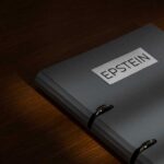 A gray folder labeled 'EPSTEIN' resting on a wooden surface