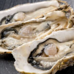 Three open oysters on a dark wooden surface