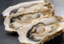 Three open oysters on a dark wooden surface