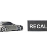 RECALL: Deadly Transmission TRAP — 1.4M Vehicles A miniature gray sports car next to a black sign that reads 'RECALL'