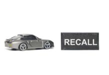 A miniature gray sports car next to a black sign that reads 'RECALL'