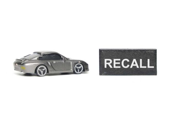 A miniature gray sports car next to a black sign that reads 'RECALL'