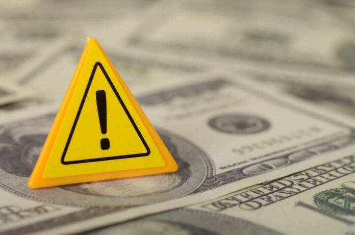 A yellow warning sign placed on a pile of dollar bills