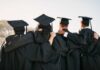 Group of graduates standing together with arms around each other, wearing caps and gowns