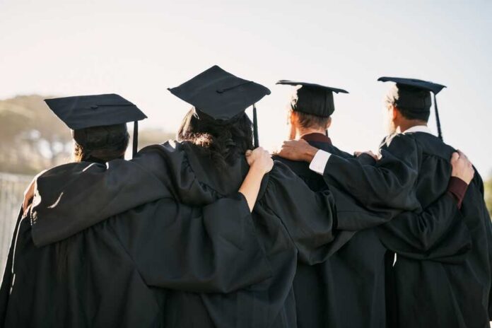 Group of graduates standing together with arms around each other, wearing caps and gowns