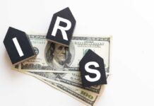 Blocks spelling 'IRS' placed on top of hundred dollar bills featuring Benjamin Franklin