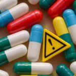 Drug Giant Caves — Trump’s Leverage Changes Everything Colorful capsules scattered around a yellow warning sign