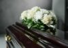 A floral arrangement of white roses and greenery on a polished casket
