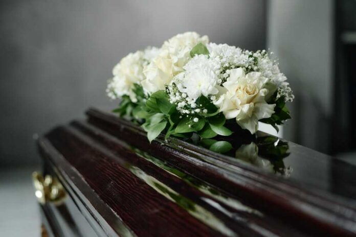 shutterstock_2684119431.jpg A floral arrangement of white roses and greenery on a polished casket