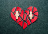 A broken heart made of red paper with wooden figures representing a couple