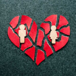 A broken heart made of red paper with wooden figures representing a couple