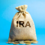 A burlap bag labeled 'IRA' with coins scattered around it