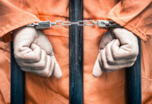 259-Year Sentence? University Shooter’s Fate Looms Handcuffed person in orange jumpsuit behind prison bars.