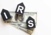 Blocks spelling 'IRS' placed on top of hundred dollar bills featuring Benjamin Franklin