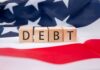 American Dream COLLAPSING Under Record Debt Load Wooden blocks spelling 'DEBT' on an American flag background